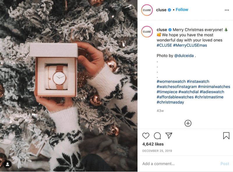Instagram-Post von @cluse zeigt ein Bild eines Modells mit Schneeflockenpullover, das eine Uhr vor einem schneebedeckten Baum von @dulceida mit den Hashtags #cluse und #meryclusemas hält